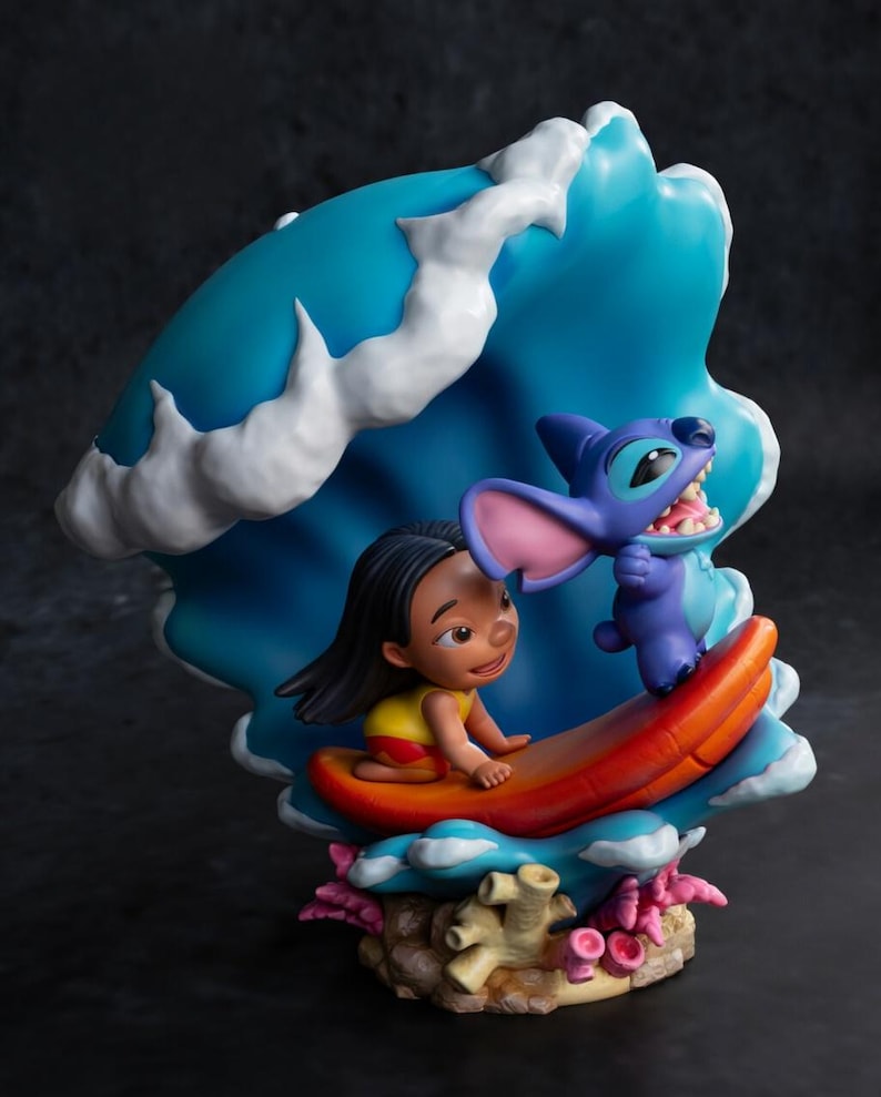 May include: A colorful figurine featuring Lilo and Stitch. Lilo is on a surfboard, and Stitch is next to her. The background is a blue wave with white accents. The base has coral and other sea elements. The figurine is a vibrant display of the characters.