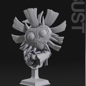May include: A gray bust of a mask with large eyes, a detailed face, and spiky protrusions. The mask is mounted on a square pedestal. The word "BUST" is printed vertically on the right side of the image.