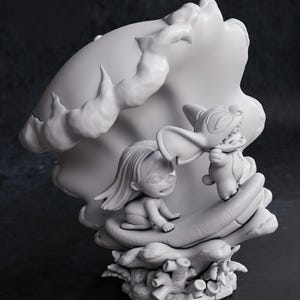 May include: A grayscale figurine featuring a young girl and a cartoon character. The girl is seated, and the character is standing, both within a large, stylized seashell. The base includes coral-like elements. The text "CHIBI TURNTABLE" is visible.