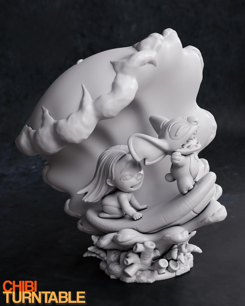 May include: A grayscale figurine featuring a young girl and a cartoon character. The girl is seated, and the character is standing, both within a large, stylized seashell. The base includes coral-like elements. The text "CHIBI TURNTABLE" is visible.