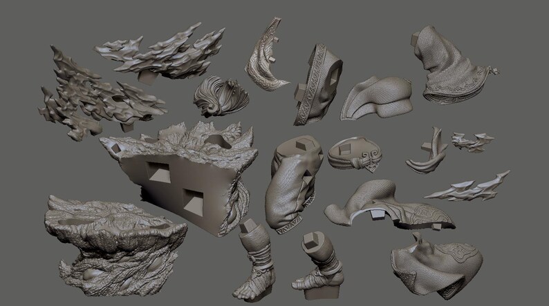 May include: A collection of gray 3D-printed model parts, including architectural elements, organic shapes, and stylized figures. The pieces vary in size and detail, with rough textures and intricate designs. The objects are arranged against a neutral gray background.
