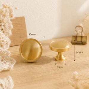 May include: Two round, brushed gold-tone metal cabinet knobs. One knob is shown from the top, and the other is shown from the side. The diameter is 30mm, the height is 24mm, and the base diameter is 15mm as indicated by the text labels.