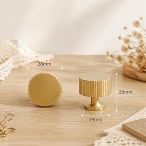 May include: Two circular brass cabinet knobs with a ribbed side texture. One knob is shown from the top, and the other is shown from the side. The knobs have a diameter of 28mm, a height of 28mm, and a base diameter of 19mm as indicated by labels.