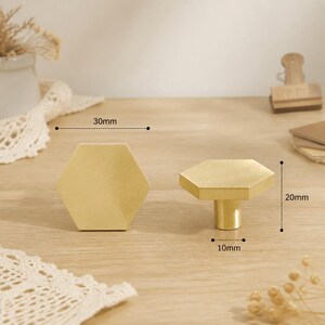 May include: Two hexagonal brass cabinet knobs with a brushed finish. One knob is shown from the front, and the other is shown from the side. The width is 30mm, the total height is 20mm, and the base diameter is 10mm as indicated by labels.
