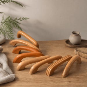 Könnte beinhalten: Eine Sammlung von sechs gewölbten Schrankgriffen aus Holz, die in einer Reihe angeordnet sind. Die Griffe haben eine glatte, hellbraune Oberfläche mit unterschiedlichen Maserungen. Jeder Griff hat zwei Befestigungspunkte an der Basis.