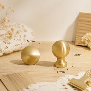 May include: Two brushed gold metal cabinet knobs with a spherical head design. One knob is shown from the side, measuring 33mm in height and 17mm at the base, while the other is shown from the front, measuring 24mm in diameter.
