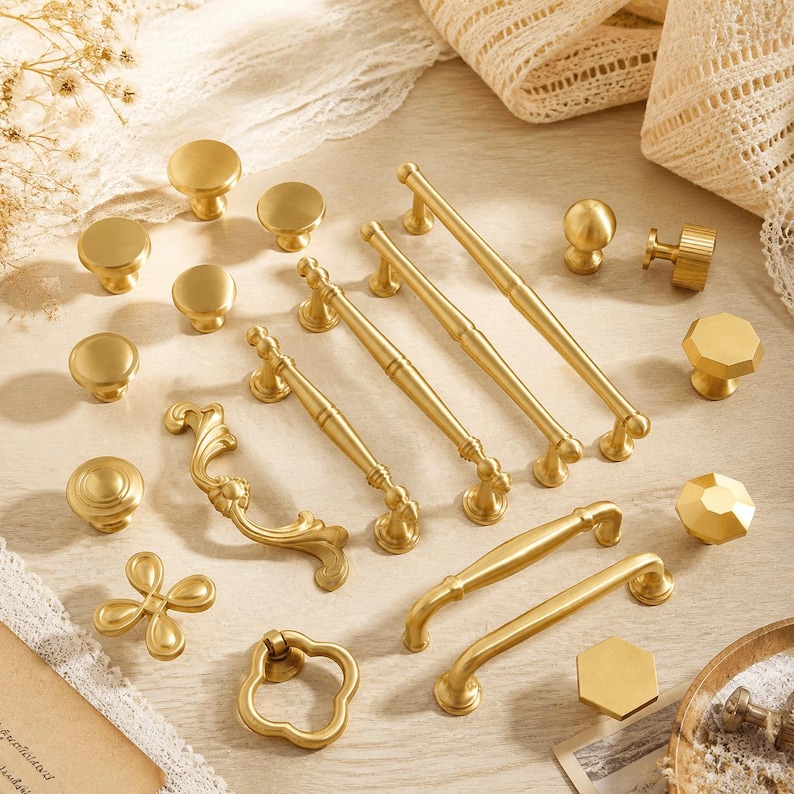 May include: A collection of gold-toned metal cabinet hardware including various drawer pulls, knobs, and handles. The set features smooth round knobs, faceted hexagonal knobs, curved ornate pulls, and straight bar handles with a brushed finish.