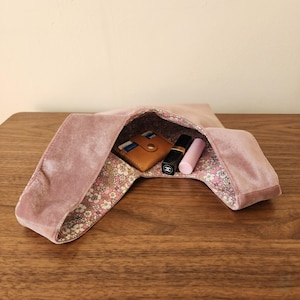 Peut inclure: Un sac hobo en velours rose poudr&eacute; avec une doublure int&eacute;rieure &agrave; motifs floraux. &Agrave; l'int&eacute;rieur du sac, on trouve un porte-cartes en cuir beige, un tube de rouge &agrave; l&egrave;vres noir avec un logo blanc et un tube de rouge &agrave; l&egrave;vres rose clair.