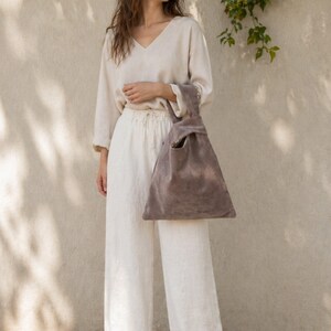 Peut inclure: Un haut beige &agrave; manches longues et col en V avec un pantalon large assorti, accompagn&eacute; d'un sac en daim taupe &agrave; poign&eacute;e nou&eacute;e. Le sac pr&eacute;sente une silhouette triangulaire avec une anse int&eacute;gr&eacute;e form&eacute;e par un n&oelig;ud et une texture mate.