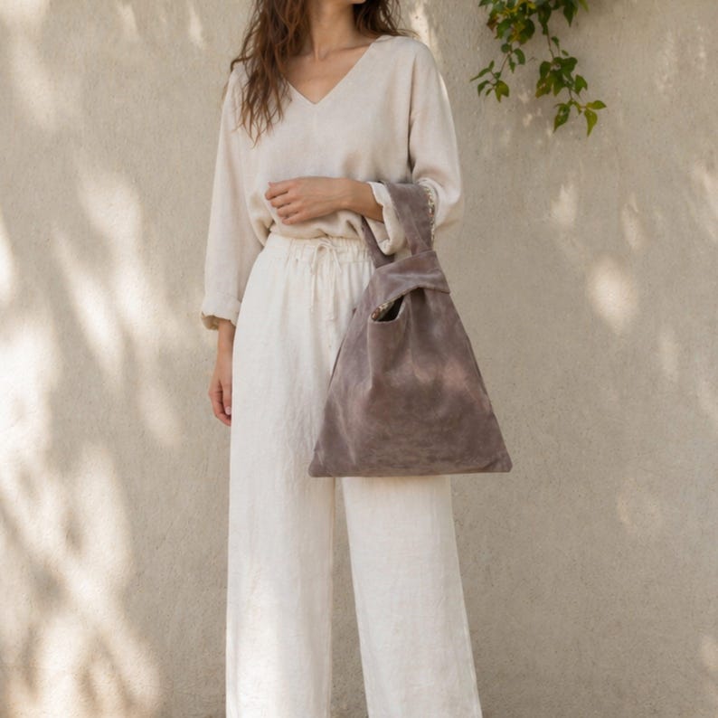 Peut inclure: Un haut beige &agrave; manches longues et col en V avec un pantalon large assorti, accompagn&eacute; d'un sac en daim taupe &agrave; poign&eacute;e nou&eacute;e. Le sac pr&eacute;sente une silhouette triangulaire avec une anse int&eacute;gr&eacute;e form&eacute;e par un n&oelig;ud et une texture mate.