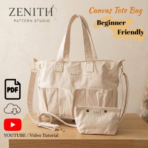 May include: Beige canvas tote bag with a matching smaller pouch. The tote has two front pockets, a shoulder strap, and top handles. The text "Canvas Tote Bag Beginner Friendly" is displayed. The bag is on a wooden surface.