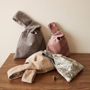 Peut inclure: Quatre petits sacs en tissu &agrave; n&oelig;ud de couleur gris, rose poudr&eacute;, beige et un motif marbr&eacute; bleu-gris. Chaque sac pr&eacute;sente une anse unique et une doublure int&eacute;rieure &agrave; motifs floraux contrastants. Un petit d&eacute; &agrave; coudre m&eacute;tallique est pos&eacute;.