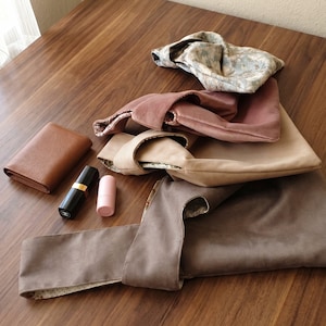 Peut inclure: Un ensemble de quatre sacs &agrave; nouer en tissu aux couleurs florales, vieux rose, beige et taupe, accompagn&eacute; d'un portefeuille en cuir marron, d'un tube de rouge &agrave; l&egrave;vres noir avec une bande dor&eacute;e et d'un petit r&eacute;cipient cylindrique rose.
