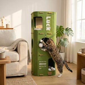 Op de afbeelding: Een groene kattenboom met meerdere niveaus, een krabpaal en een speelse kat die naar een speeltje reikt. De kattenboom heeft het woord "LUCK" aan de zijkant en de tekst "Hold the chow shovel shit to the oid".