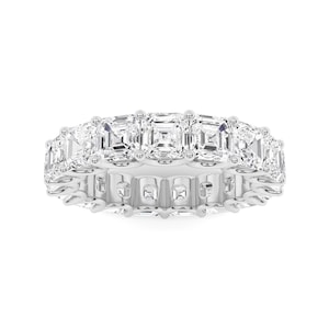May include: A white gold eternity ring featuring a continuous row of square-cut, clear gemstones. The ring's band is a polished, bright metal, and the gemstones are set closely together, creating a sparkling, elegant appearance. This ring is a piece of fine jewelry.