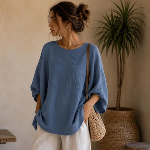 May include: A loose-fitting blue top with three-quarter length sleeves and a round neckline, paired with white, wide-leg trousers that feature gathered, elasticised cuffs at the ankles. A woven straw shoulder bag is worn over the shoulder.