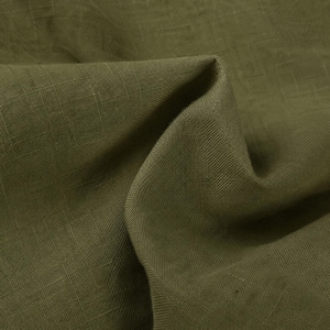 May include: A piece of olive green fabric with a visible woven texture. The material is folded to create soft, deep shadows and highlights across the surface, showcasing the natural weave pattern and the consistent, earthy tone of the textile.