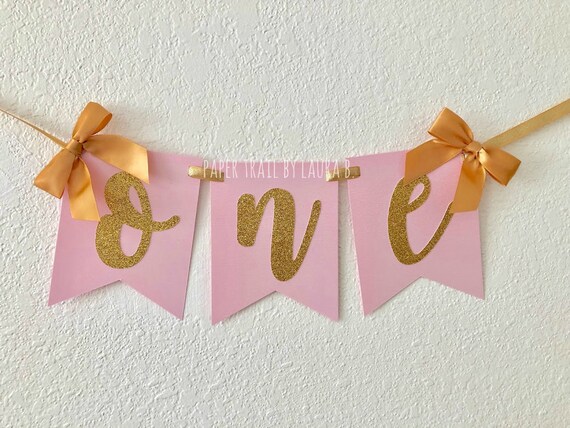 One Birthday High Chair Banner In Pink And Gold With Cursive Font
