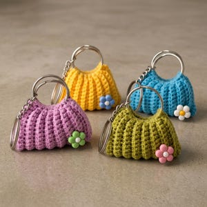 May include: Four crochet purse keyrings in shades of purple, yellow, blue, and green. Each has a silver key ring and a decorative flower. The keyrings are handmade and have a textured appearance, perfect for adding a touch of colour.