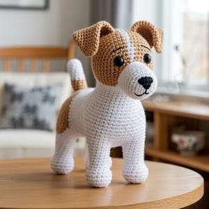 Op de afbeelding: Een gehaakte hondenfiguur in wit, bruin en zwart, staand op een houten tafel. De hond heeft een witte vacht, bruine oren en vlekken, en zwarte ogen en neus. De hond is ongeveer 20 cm hoog.