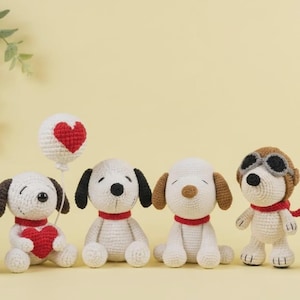 Könnte beinhalten: Gehäkelte Snoopy-Plüschtiere in Weiß, Schwarz und Braun. Eines hält ein rotes Herz, ein anderes einen Ballon mit rotem Herz, und ein weiteres trägt eine Fliegerbrille. Alle haben rote Kragen. Eine charmante Sammlung.