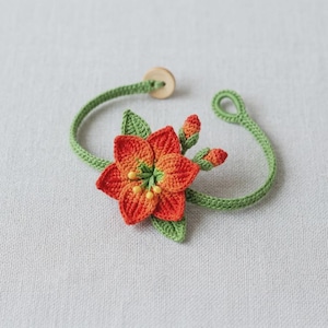 May include: A handmade crochet bracelet featuring a vibrant orange and yellow flower with green leaves and buds. The bracelet has a green band and a wooden button closure. The floral design is detailed and intricate, showcasing the artistry of the craft.