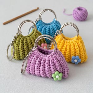 May include: Four miniature crochet purses in green, blue, yellow, and purple, each with a silver ring and chain. Decorative flower accents adorn some purses. A wooden crochet hook and a ball of purple yarn are also present.