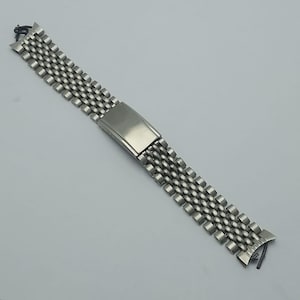 May include: A silver-toned watch band with a mesh design. The band features a rectangular clasp and a series of small, interconnected links. The band is designed to attach to a watch face and is made of a shiny, metallic material.