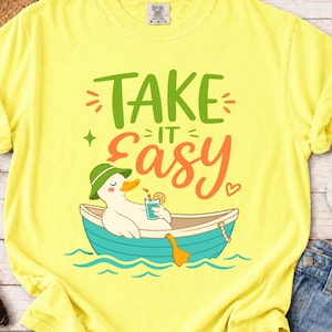 May include: Yellow t-shirt with the phrase "Take it Easy" in green and orange lettering. A cartoon duck wearing a green hat and holding a drink is in a blue boat. The duck is floating on blue water.