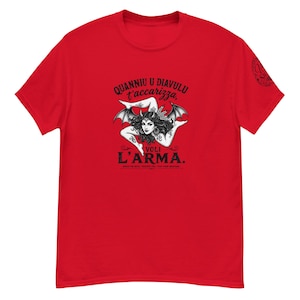Può includere: T-shirt rosso con un'illustrazione in bianco e nero di una donna alata e testo in italiano. Il testo recita "Quanniu u diavulu t'accarizza, voli l'arma."