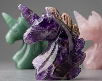 May include: A carved amethyst unicorn figurine is the focal point, showcasing a rich purple hue with lighter streaks. A green and a pink unicorn figurine are slightly out of focus in the background. The figurines are likely decorative items.