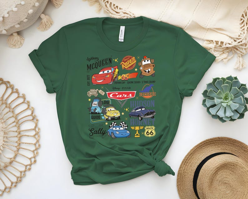May include: Green t-shirt featuring characters from the Disney Pixar Cars movie. The design includes Lightning McQueen, Mater, and other characters, along with the Cars logo and Route 66 signage. The shirt is made of a soft material.