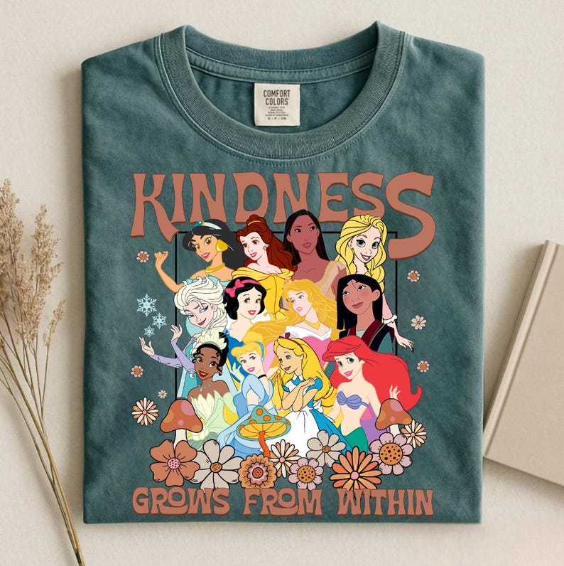 May include: Teal Comfort Colors t-shirt featuring a graphic of various cartoon princesses. The word "KINDNESS" is printed above the princesses, and "GROWS FROM WITHIN" is printed below. The design includes flowers and mushrooms.