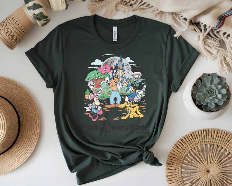 Puede incluir: Camiseta verde oscuro con un gr&aacute;fico colorido de personajes de Disney, incluyendo Mickey Mouse, Donald Duck y Goofy, frente a un castillo y el texto "Walt Disney World". La camiseta est&aacute; hecha de material suave.