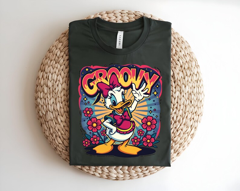 May include: Dark green t-shirt featuring a cartoon Daisy Duck design with the word "GROOVY" in a retro font. Daisy is wearing a pink bow and vest, surrounded by flowers and a burst of stars.