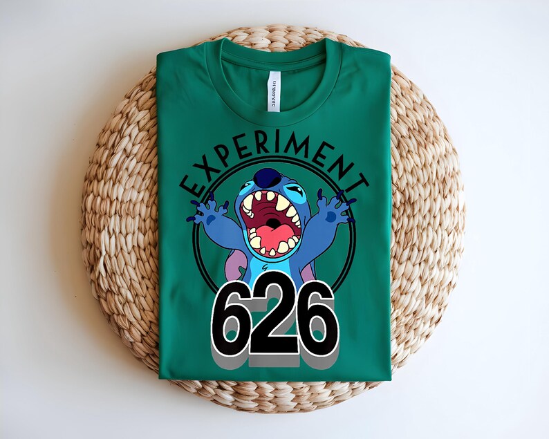 Pu&ograve; includere: Maglietta verde con un personaggio dei cartoni animati blu con la bocca aperta e le braccia alzate. Il testo "EXPERIMENT" &egrave; sopra e il numero "626" sotto.