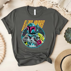 May include: Dark grey t-shirt with a vibrant graphic of Boba Fett from Star Wars. The design showcases a detailed illustration of the character with a blaster, set against a space backdrop, and the words "STAR WARS" in yellow.