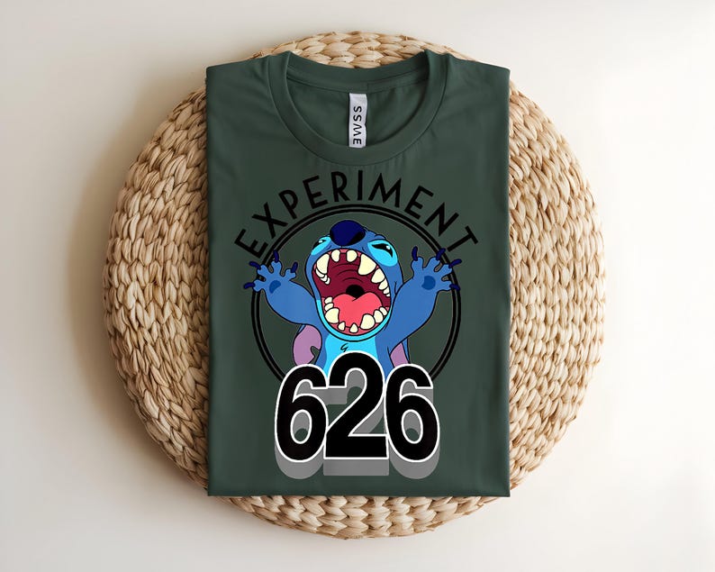 Pu&ograve; includere: T-shirt verde scuro con un personaggio dei cartoni animati blu, a bocca aperta, e la scritta "EXPERIMENT" sopra e "626" sotto. Il personaggio &egrave; all'interno di un cerchio nero.