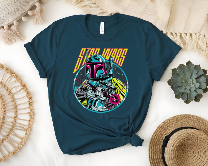 May include: Teal t-shirt with a Star Wars graphic. The design features Boba Fett in a circular image, with a helmet, blaster, and the words "STAR WARS" in yellow and pink. The shirt is made of a soft material.