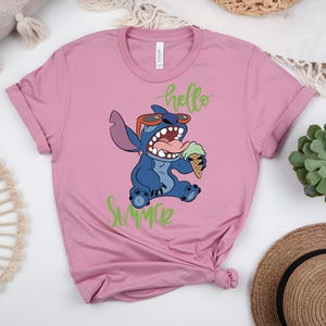 K&ouml;nnte beinhalten: Rosafarbenes T-Shirt mit einem Cartoon-Charakter, Stitch, der eine Sonnenbrille tr&auml;gt und Eis isst. Die Worte "hello Summer" stehen in gr&uuml;ner Schrift &uuml;ber und unter der Figur. Das Shirt hat kurze &Auml;rmel und einen Rundhalsausschnitt.