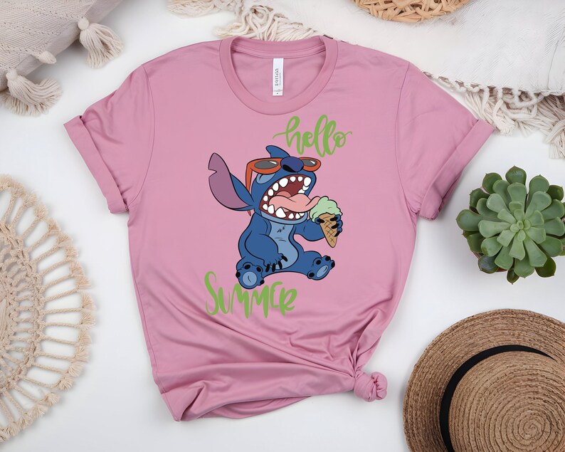 K&ouml;nnte beinhalten: Rosafarbenes T-Shirt mit einem Cartoon-Charakter, Stitch, der eine Sonnenbrille tr&auml;gt und Eis isst. Die Worte "hello Summer" stehen in gr&uuml;ner Schrift &uuml;ber und unter der Figur. Das Shirt hat kurze &Auml;rmel und einen Rundhalsausschnitt.
