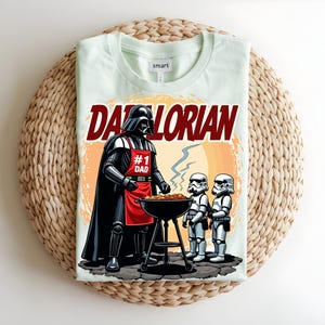May include: A pale green t-shirt with a graphic of Darth Vader wearing a red apron that says "#1 Dad" grilling with two Stormtroopers. The shirt has the word "Darthlorian" in red text.