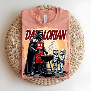 May include: A peach-coloured t-shirt with a graphic of Darth Vader grilling with Stormtroopers. The text "Darthlorian" is above the image. Darth Vader wears a red apron that says "#1 Dad".