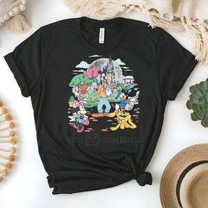 Puede incluir: Camiseta negra con un gr&aacute;fico colorido de personajes de Disney, incluyendo Mickey Mouse, Goofy y Donald Duck, frente a un castillo y el texto "Walt Disney World". El dise&ntilde;o est&aacute; impreso en una camiseta negra de cuello redondo.