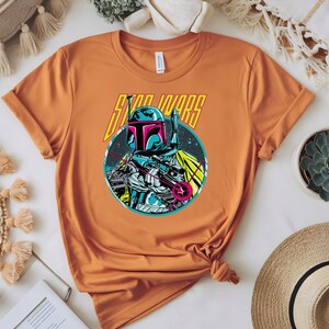 May include: Orange t-shirt with a graphic of a Star Wars character in blue, pink, and white, and the words "STAR WARS" in yellow. The t-shirt is knotted at the bottom.