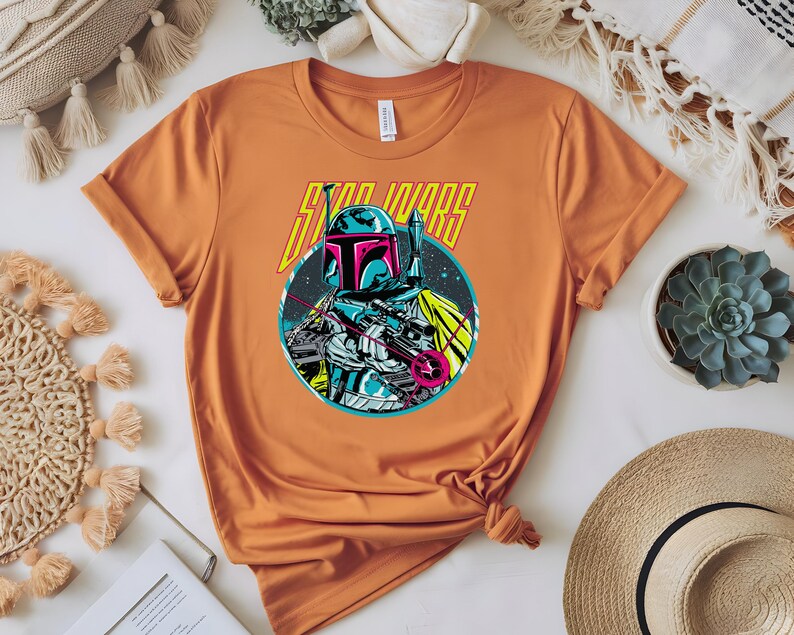 May include: Orange t-shirt with a graphic of a Star Wars character in blue, pink, and white, and the words "STAR WARS" in yellow. The t-shirt is knotted at the bottom.
