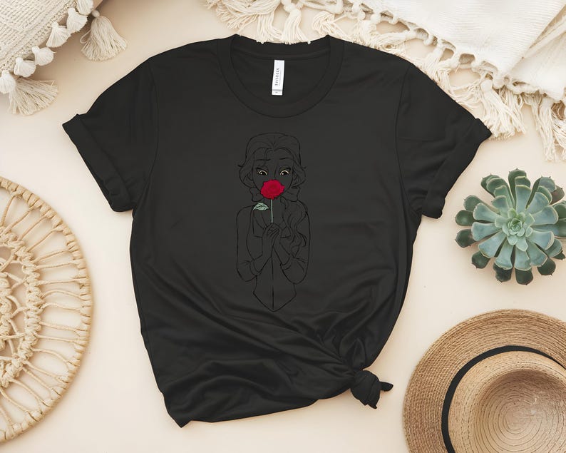 May include: Black t-shirt featuring a line drawing of a person holding a red rose. The design is a simple outline with the rose in full color. The shirt is made of a soft material and has short sleeves.