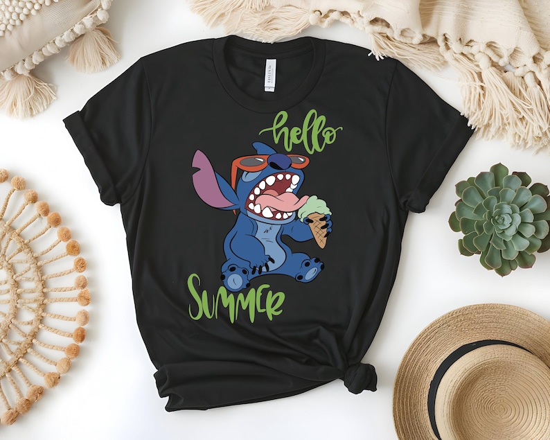 K&ouml;nnte beinhalten: Schwarzes T-Shirt mit einer Comicfigur, die eine Sonnenbrille tr&auml;gt und eine Eist&uuml;te h&auml;lt. Die Worte "hello summer" sind in gr&uuml;ner Schrift &uuml;ber und unter der Figur geschrieben.
