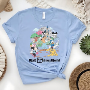Puede incluir: Camiseta azul claro con un gr&aacute;fico colorido de personajes de Disney frente al castillo de Cenicienta. El texto "Walt Disney World" est&aacute; impreso en negro. La camiseta est&aacute; hecha de un material suave.
