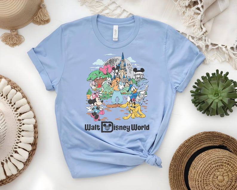 Puede incluir: Camiseta azul claro con un gr&aacute;fico colorido de personajes de Disney frente al castillo de Cenicienta. El texto "Walt Disney World" est&aacute; impreso en negro. La camiseta est&aacute; hecha de un material suave.